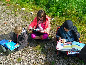 3 enfants qui lisent assis dans le jardin